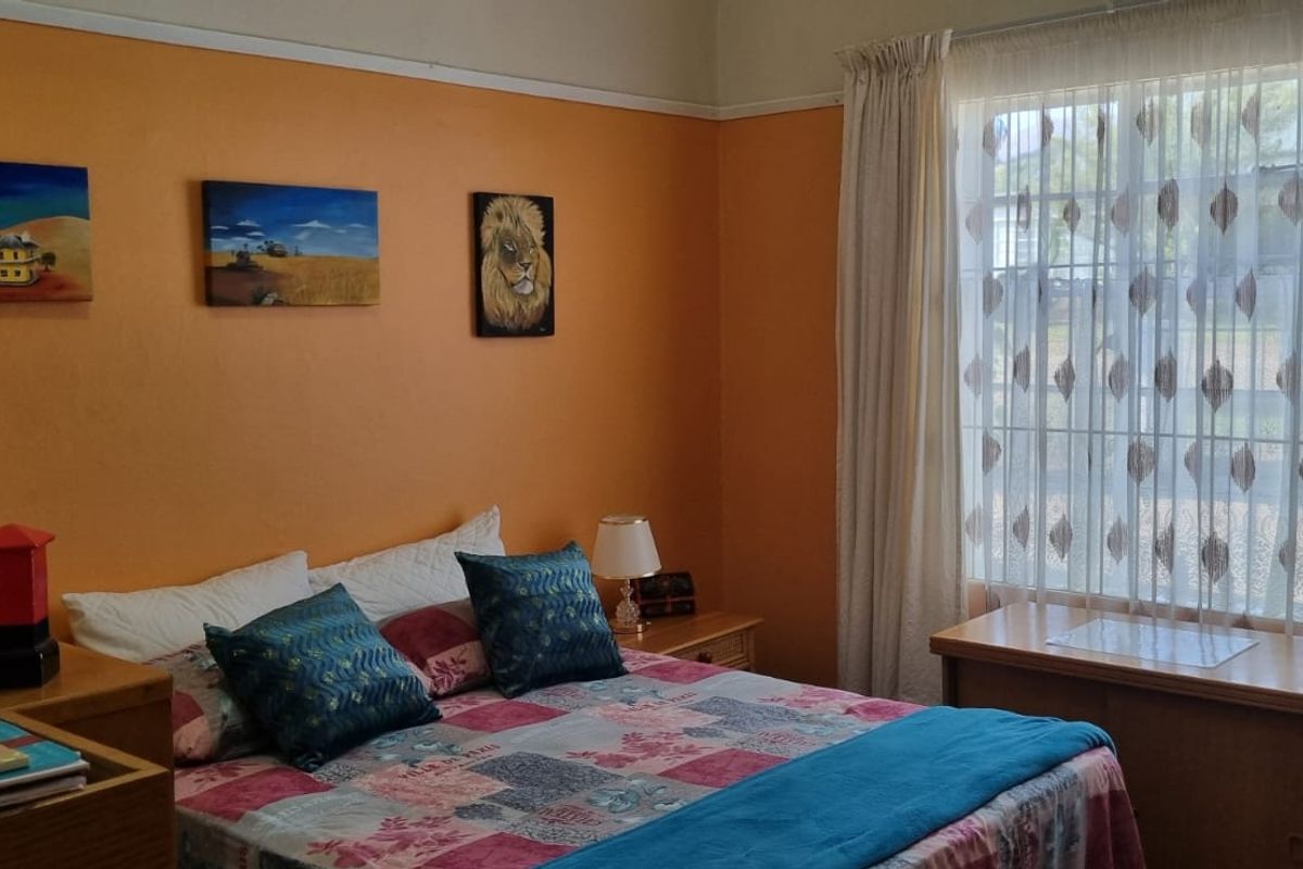A bedroom featuring orange walls, a large window with curtains, and a picture rail.