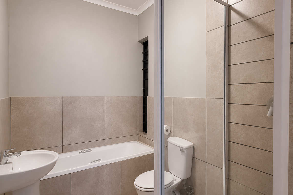 A clean, modern bathroom featuring a pedestal basin, built-in bathtub, toilet, and a glass-enclosed shower with neutral-toned wall and floor tiling.