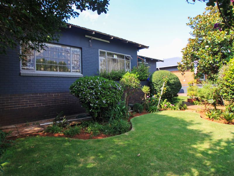 A view of the rear exterior of the house featuring a painted brick facade, steel-framed windows, and a well-maintained garden area.