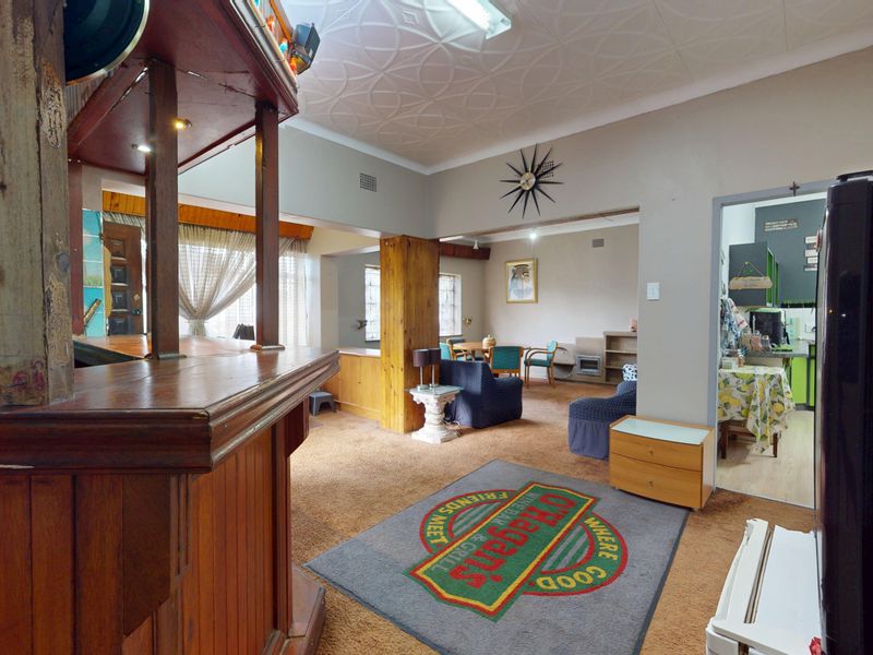 A spacious interior area featuring a built-in wooden bar counter, textured ceiling tiles, and an open-plan layout connecting to adjacent living and kitchen spaces.