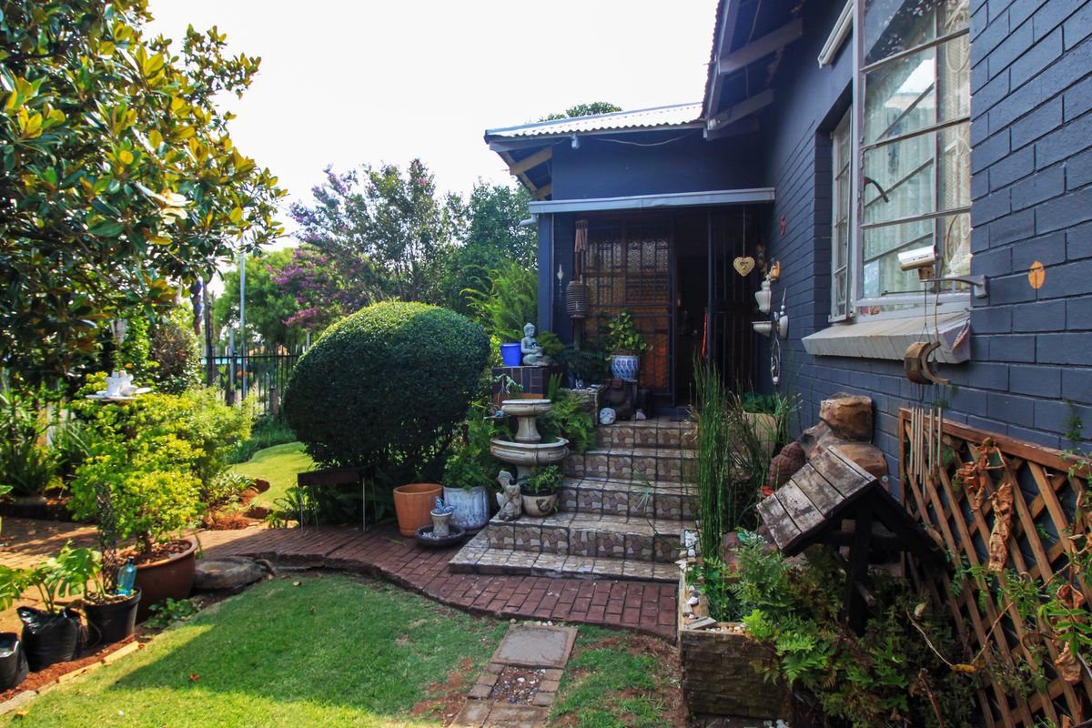 A charming rear exterior view featuring a dark-painted brick facade, tiled entrance steps, and a well-maintained landscaped garden with brick pathways.