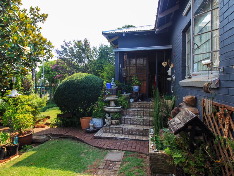 A charming rear exterior view featuring a dark-painted brick facade, tiled entrance steps, and a well-maintained landscaped garden with brick pathways.