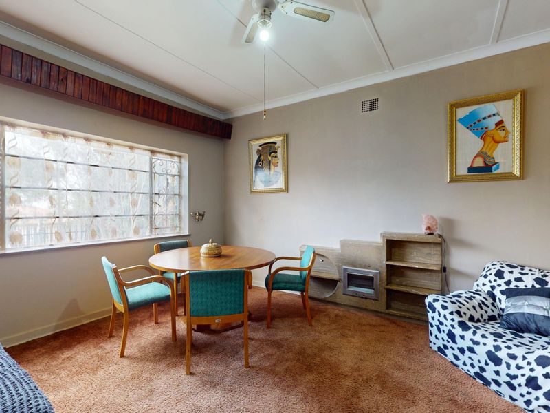A living room featuring a built-in fireplace, integrated shelving, and a ceiling fan, with large windows fitted with security bars.