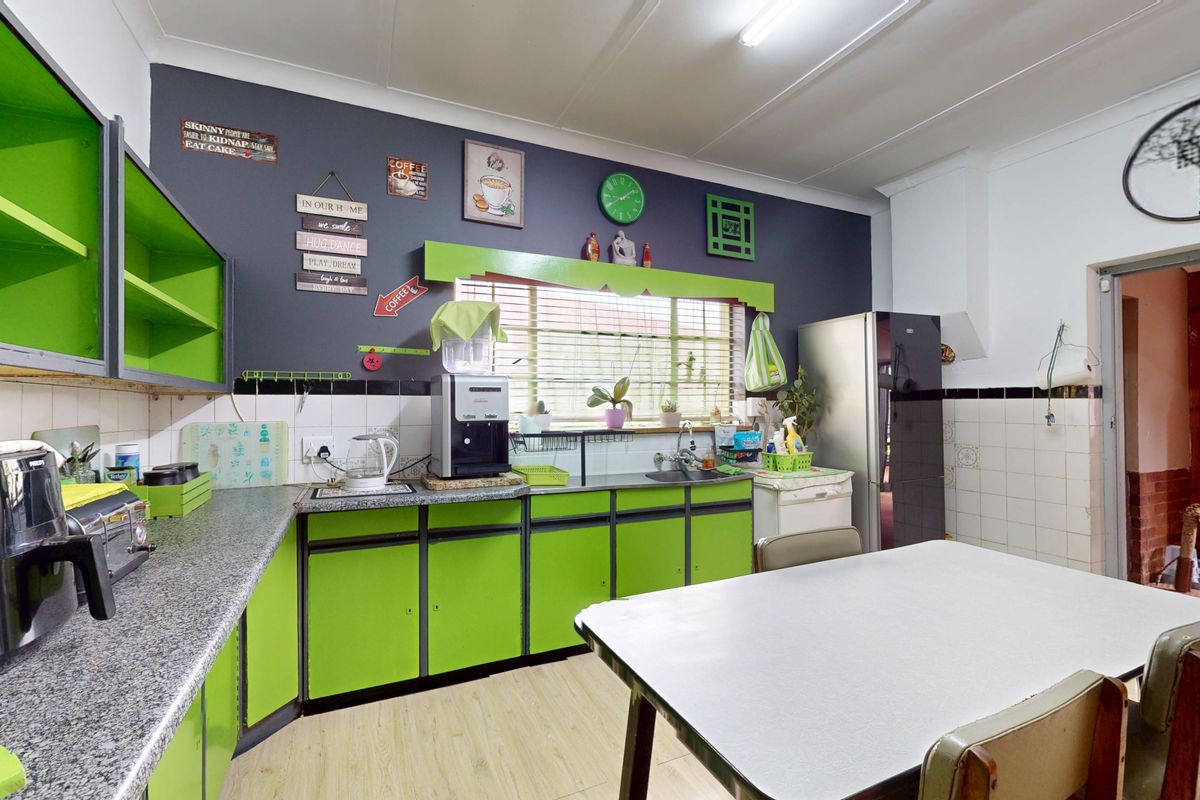 A functional kitchen featuring bright green cabinetry, laminate countertops, a tiled backsplash, and a window with venetian blinds.