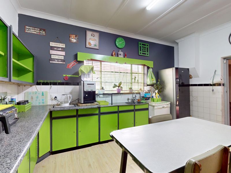 A functional kitchen featuring bright green cabinetry, laminate countertops, a tiled backsplash, and a window with venetian blinds.