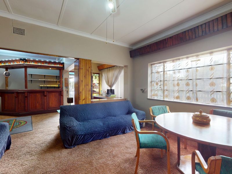 Open plan living and dining area featuring a built-in bar, large windows with security bars, and carpeted flooring throughout.