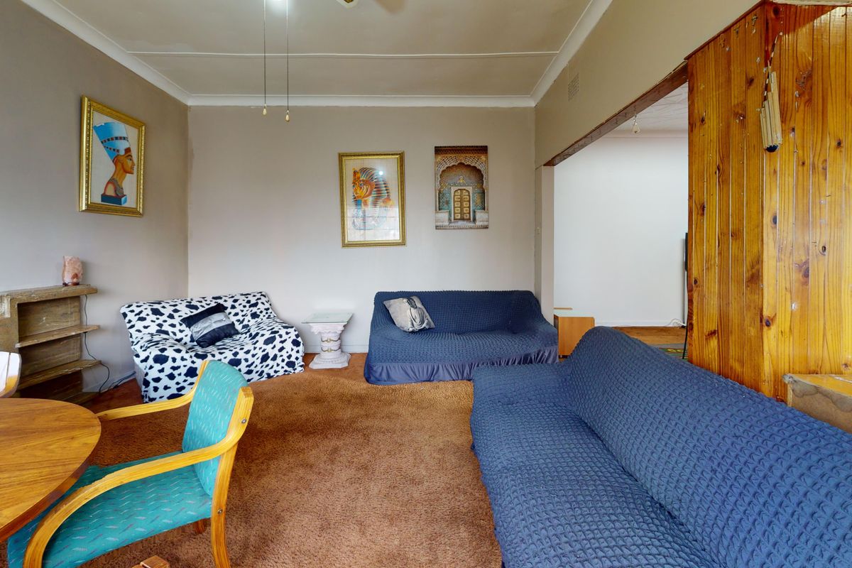A living room featuring brown carpet flooring, coving, and timber wall paneling, offering a dated interior space ready for modernization.