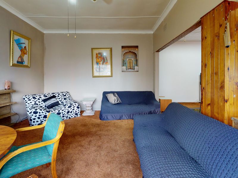 A living room featuring brown carpet flooring, coving, and timber wall paneling, offering a dated interior space ready for modernization.