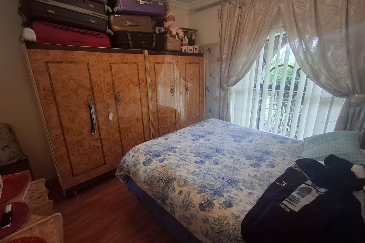 A bedroom featuring a large built-in wardrobe with wood-grain finish, laminate flooring, and vertical blinds covering the window.