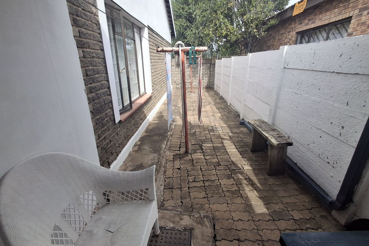 A narrow rear exterior walkway featuring paved flooring and a white precast concrete boundary wall, showing signs of wear and weathering.