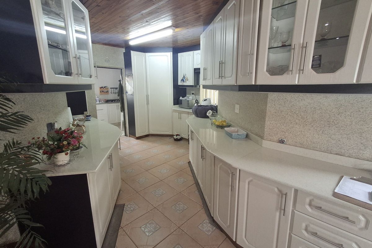 A functional kitchen featuring extensive built-in cabinetry, stone countertops, tiled flooring, and a timber-clad ceiling, offering ample storage and workspace.
