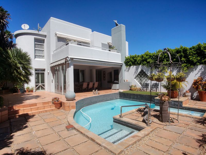 Rear exterior view featuring a swimming pool, paved patio area, covered terrace, and a balcony overlooking the garden.