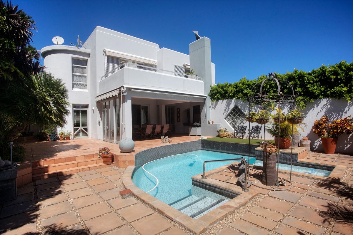 Rear exterior view featuring a swimming pool, paved patio area, covered terrace, and a balcony overlooking the garden.