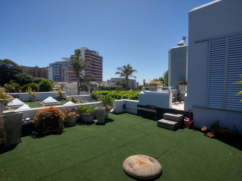 Spacious rooftop terrace featuring artificial turf, built-in masonry walls, and louvre shutters, offering an open-air outdoor living space with urban views.