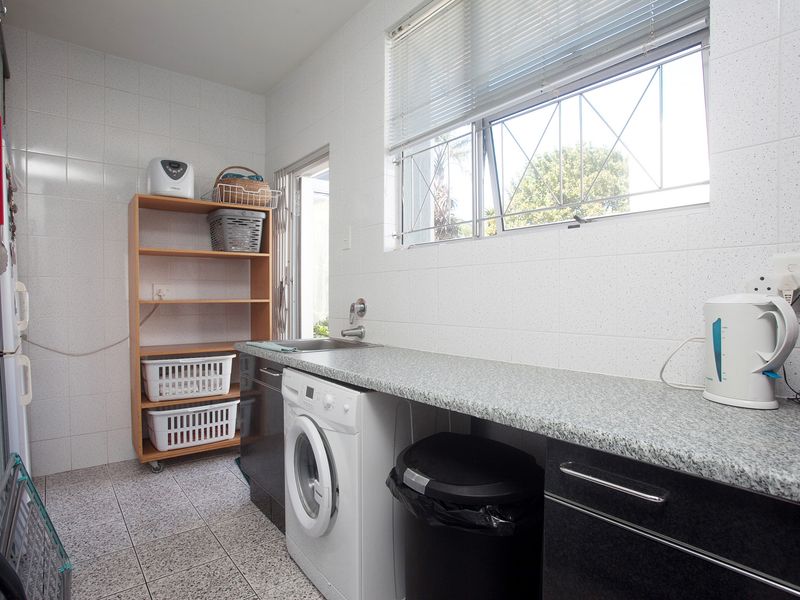 Functional laundry room featuring tiled walls and flooring, laminate countertops, a stainless steel sink, and built-in cabinetry with space for a washing machine.