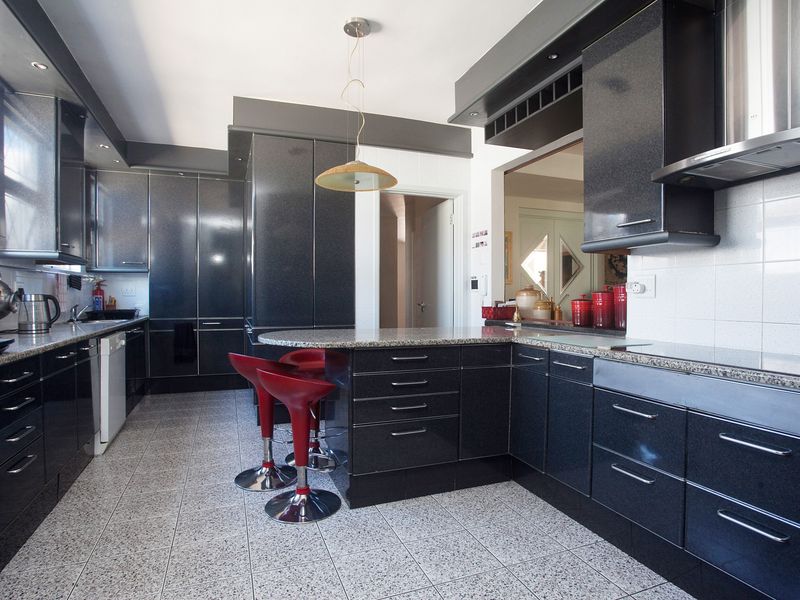 Modern kitchen featuring dark high-gloss cabinetry, granite countertops, a breakfast bar, and tiled flooring with integrated stainless steel extractor fan.