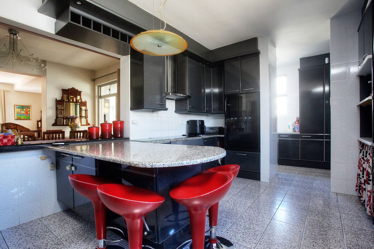 Modern kitchen featuring dark cabinetry, granite countertops, a breakfast bar, and integrated appliances, with tiled flooring and an open-plan layout.