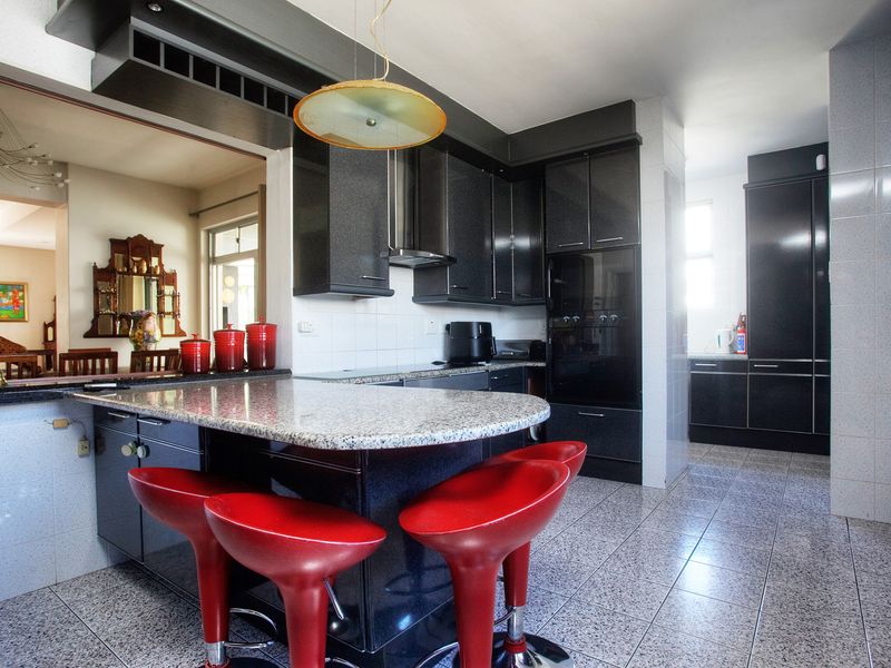 Modern kitchen featuring dark cabinetry, granite countertops, a breakfast bar, and integrated appliances, with tiled flooring and an open-plan layout.
