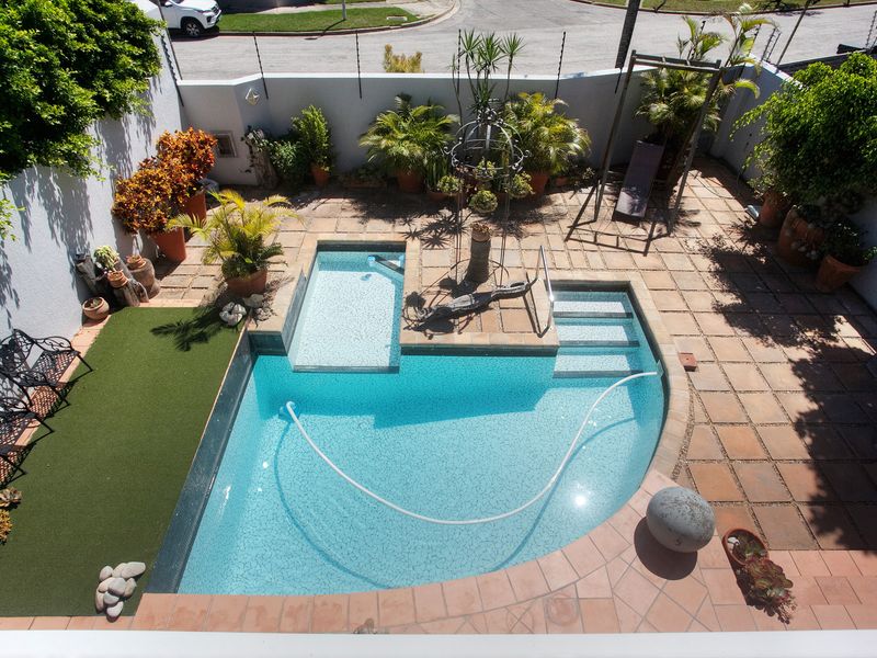 An elevated view of a private courtyard featuring a swimming pool with integrated steps, paved patio area, and artificial turf section.