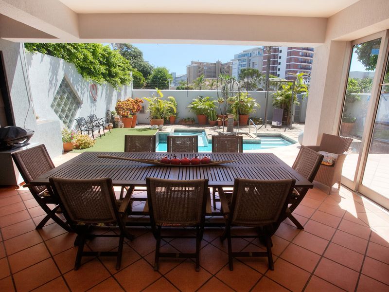 Covered outdoor patio featuring tiled flooring, overlooking a private swimming pool and garden area with direct access to the interior via sliding glass doors.