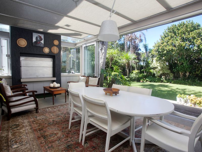 A bright, enclosed patio featuring a built-in braai, retractable glass doors, and direct access to a lush, landscaped garden.