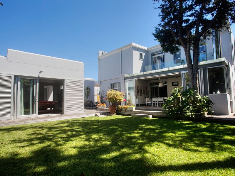Rear view of the property featuring a well-maintained lawn, timber decking, and a covered patio area with glass sliding doors.