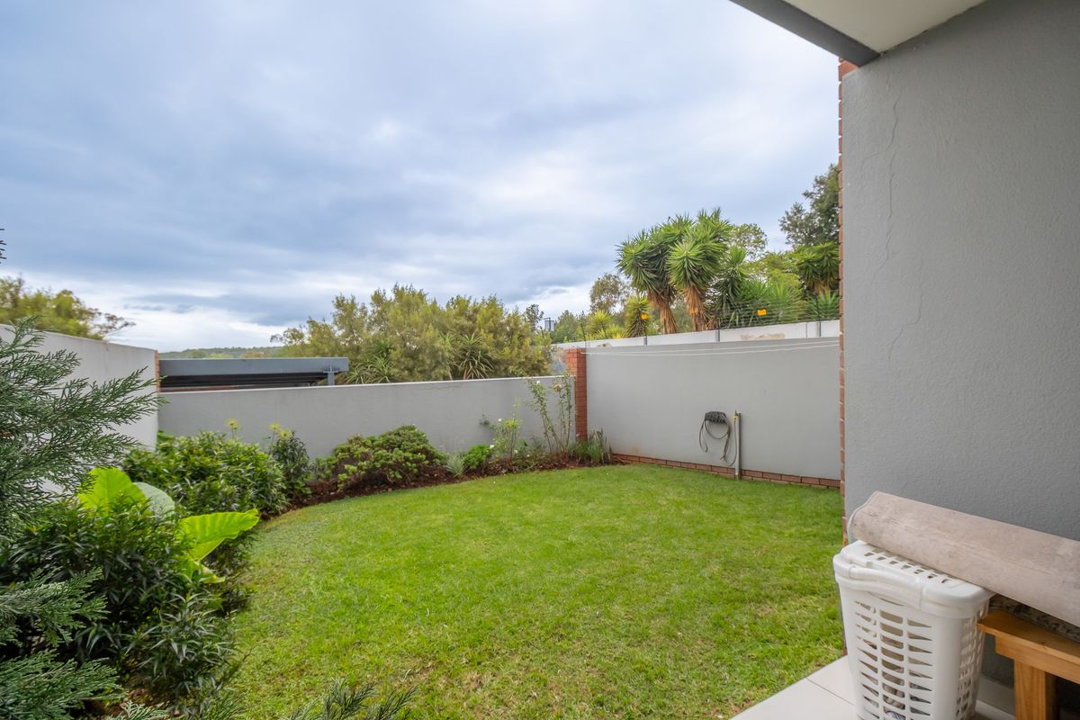 A private rear garden area featuring a manicured lawn, perimeter boundary walls, and established greenery, accessible from the apartment.