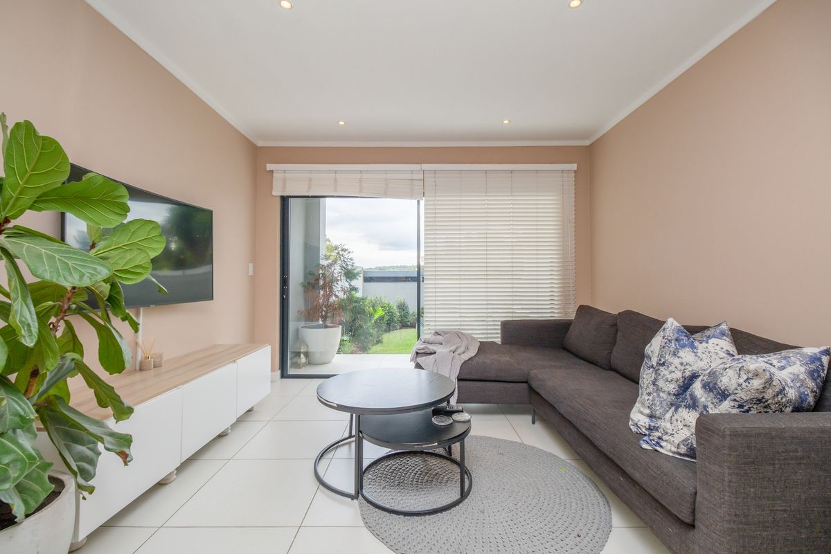 A bright living room featuring large sliding glass doors that open onto a private patio, complemented by neutral wall tones and tiled flooring.