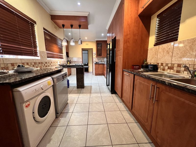 A functional kitchen featuring wooden cabinetry, granite countertops, tiled flooring, and integrated appliances, offering a practical layout with ample storage space.