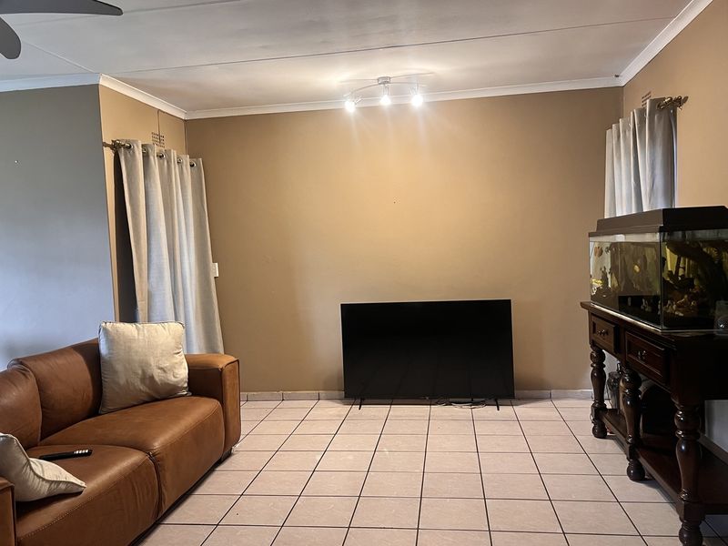 A living room featuring tiled flooring, neutral wall paint, and a ceiling fan, providing a functional and versatile space for relaxation.
