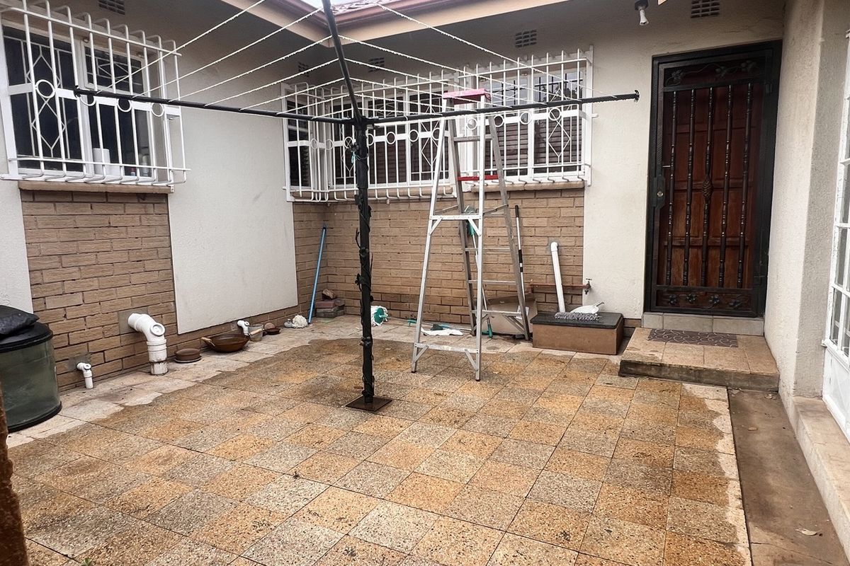 A paved rear courtyard area featuring brick wall finishes, security bars on windows, and a secure entrance door.