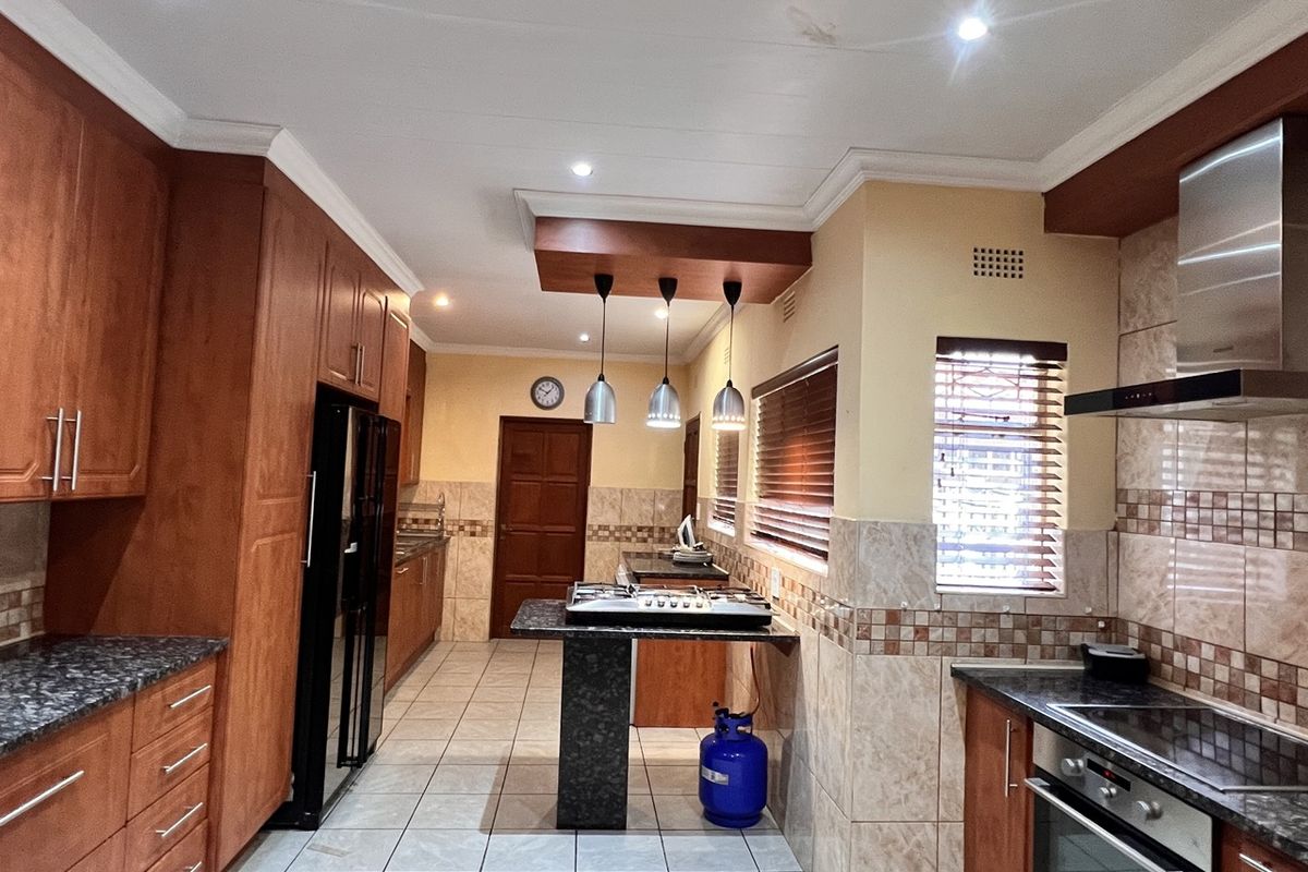Spacious kitchen featuring extensive wooden cabinetry, granite countertops, built-in oven and gas hob, tiled flooring, and modern recessed lighting.
