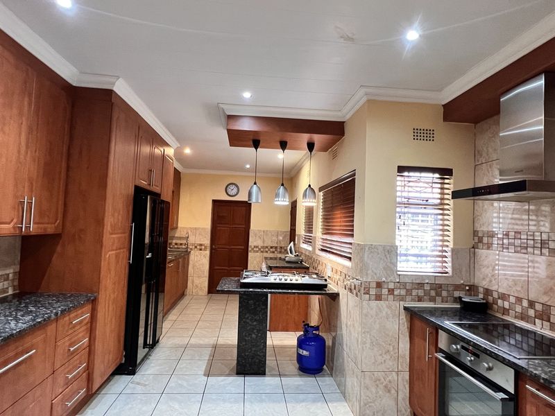 Spacious kitchen featuring extensive wooden cabinetry, granite countertops, built-in oven and gas hob, tiled flooring, and modern recessed lighting.
