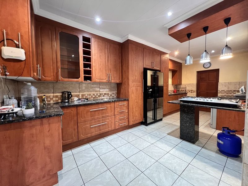 Spacious kitchen featuring warm-toned wooden cabinetry, granite countertops, tiled flooring, and a central island with a built-in gas hob and pendant lighting.