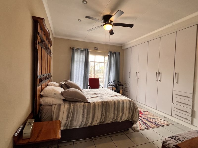 Spacious bedroom featuring extensive built-in cupboards, tiled flooring, and a central ceiling fan with integrated lighting.