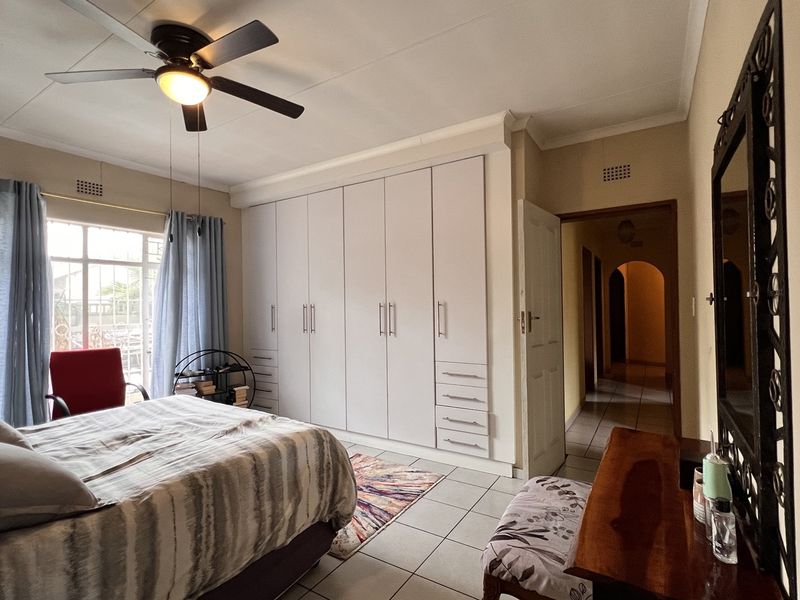 A spacious bedroom featuring extensive built-in cupboards, tiled flooring, and a ceiling fan, with direct access to the hallway.