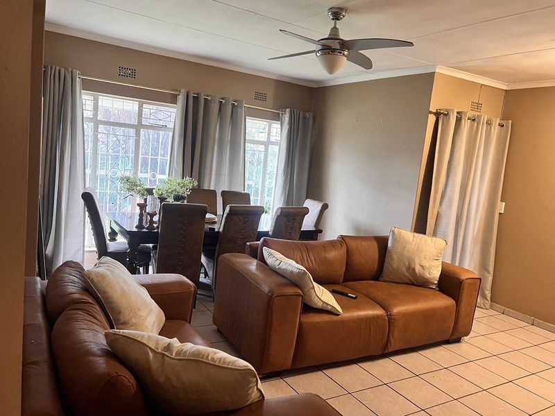 Open-plan living and dining area featuring tiled flooring, a ceiling fan, and large windows with security bars.