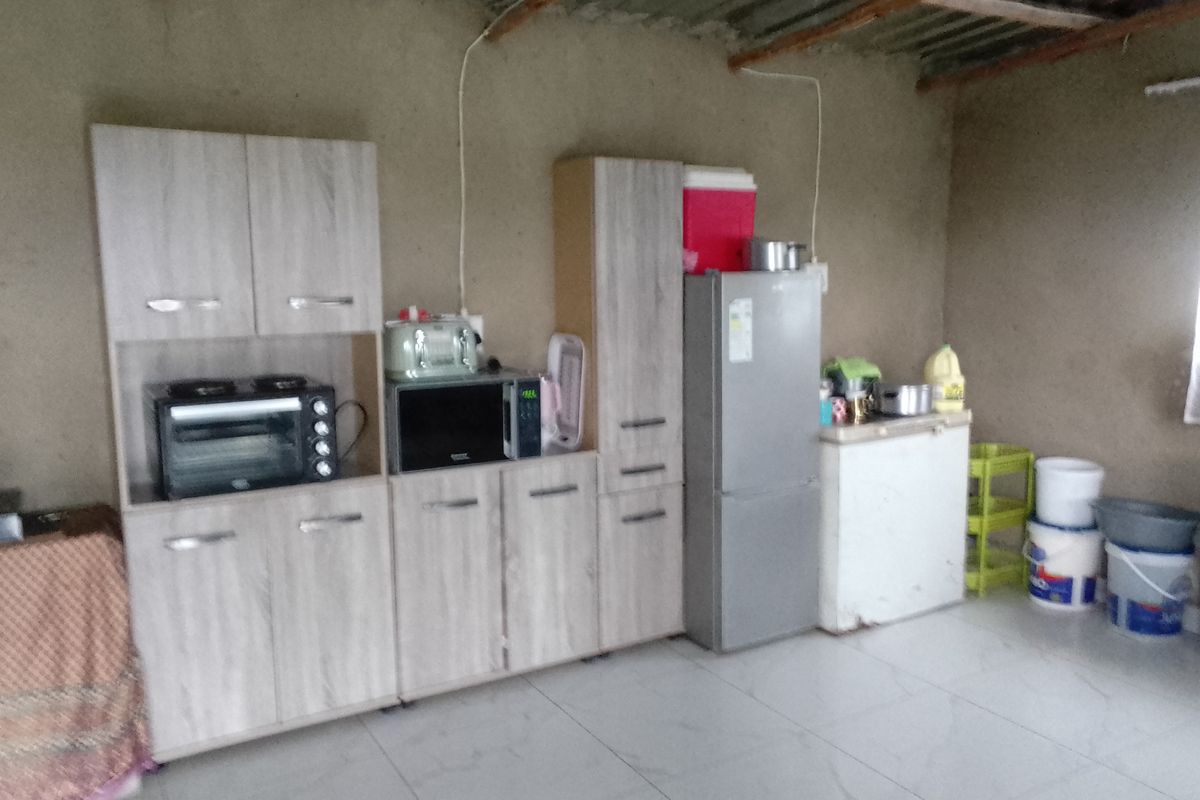 A basic kitchen area featuring light wood-look cabinetry, tiled flooring, and an exposed corrugated metal ceiling with unfinished wall finishes.