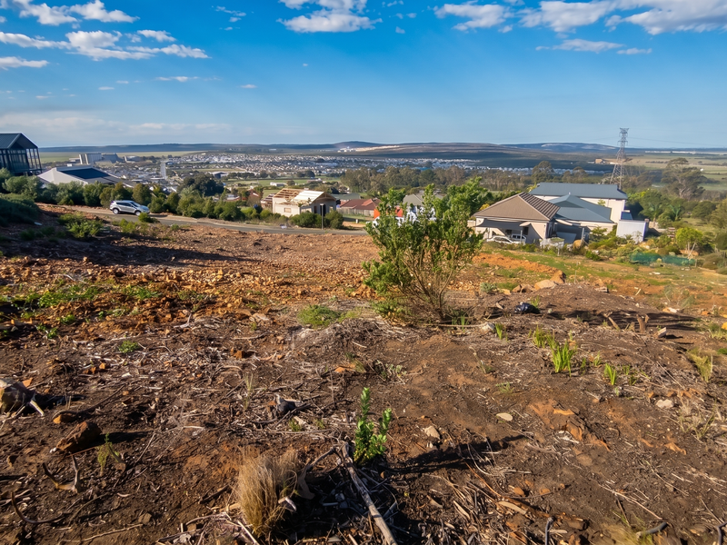 A wide-angle view overlooking a sloped residential plot with surrounding neighborhood development and distant landscape scenery.
