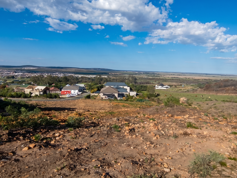 Elevated view overlooking a residential area and expansive natural landscape from a vacant residential plot.