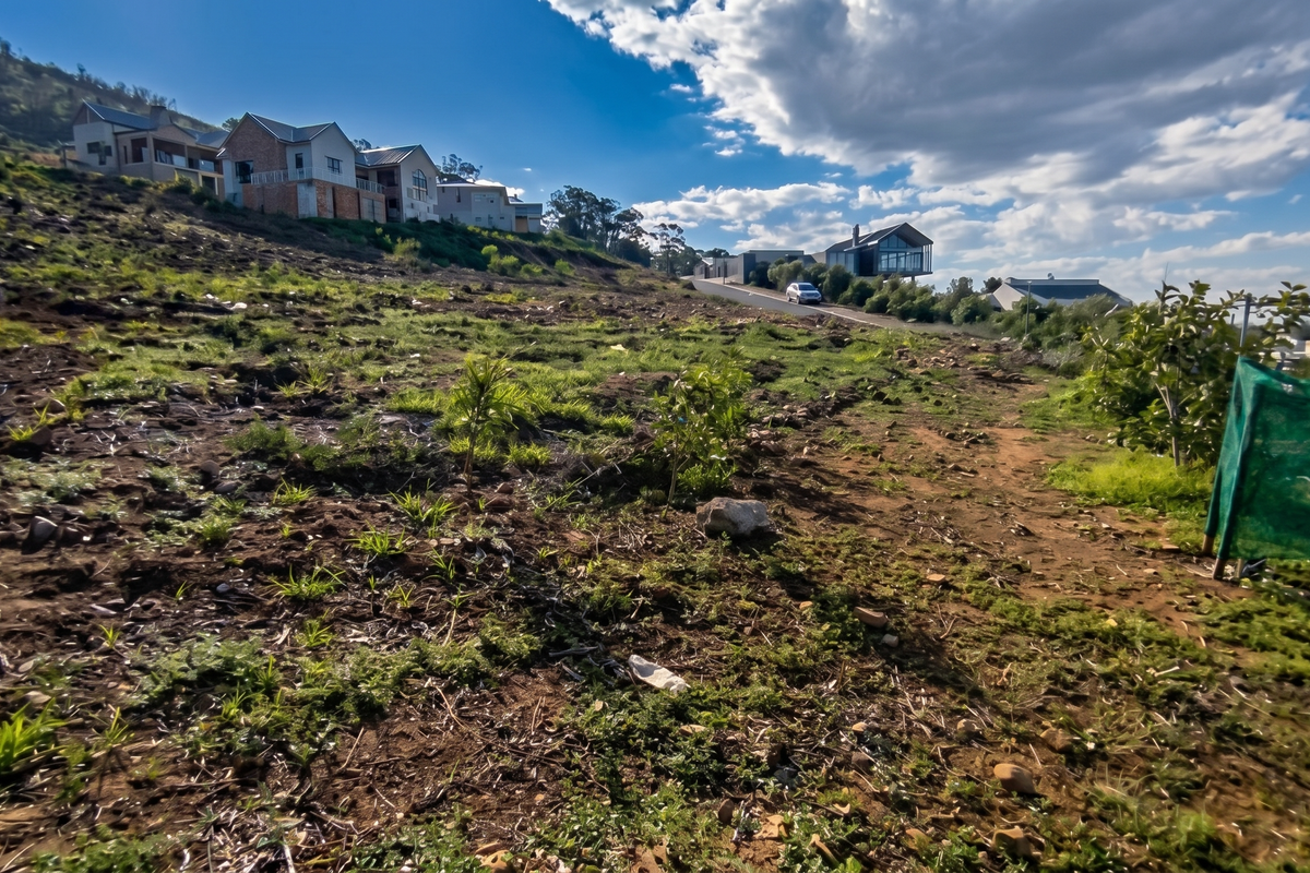 A sloped, undeveloped residential plot with natural vegetation, offering a view of neighboring hillside properties in a quiet estate setting.