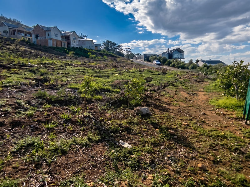 A sloped, undeveloped residential plot with natural vegetation, offering a view of neighboring hillside properties in a quiet estate setting.