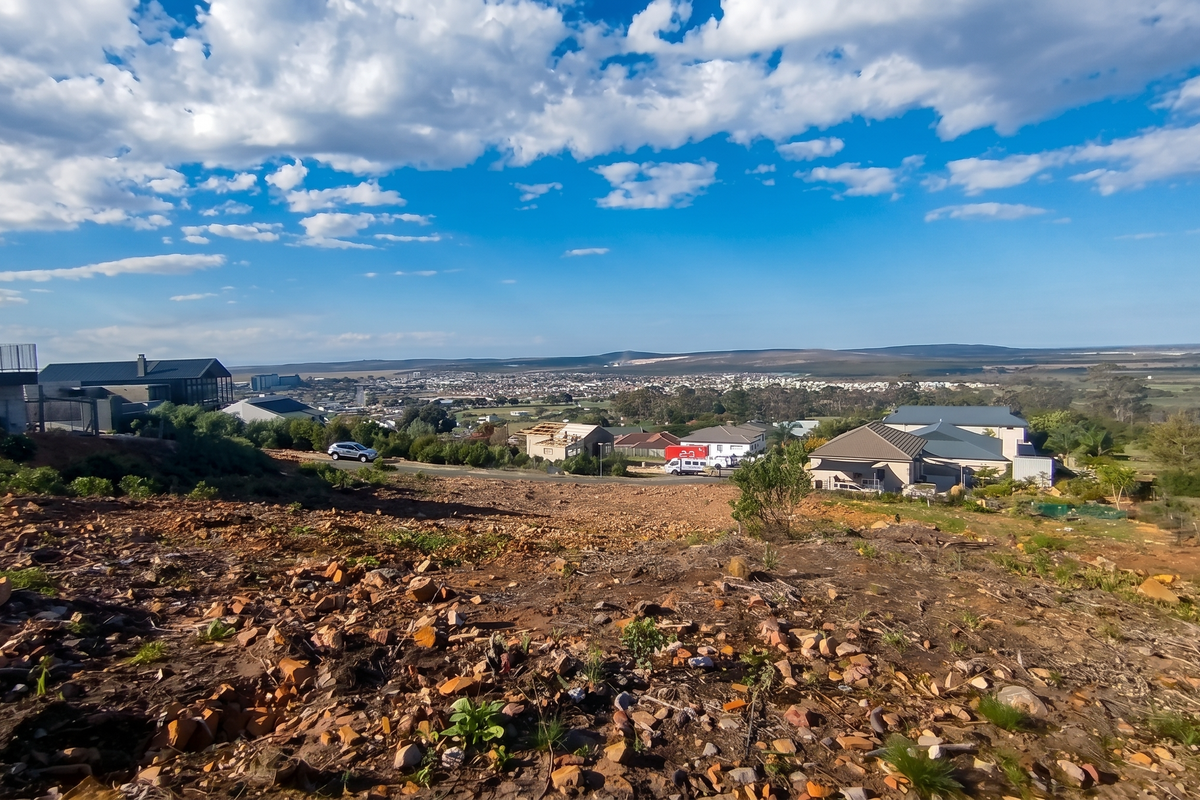 A wide-angle view overlooking a residential area from a sloped, undeveloped vacant plot of land.