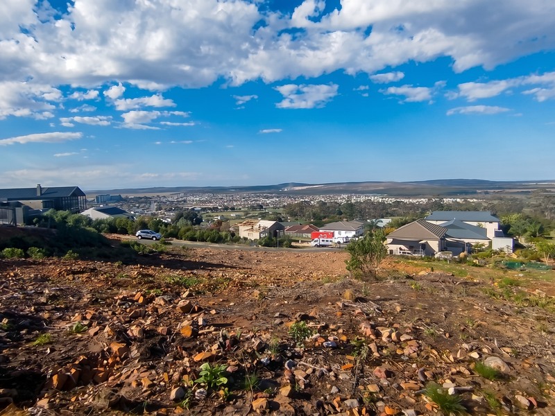 A wide-angle view overlooking a residential area from a sloped, undeveloped vacant plot of land.