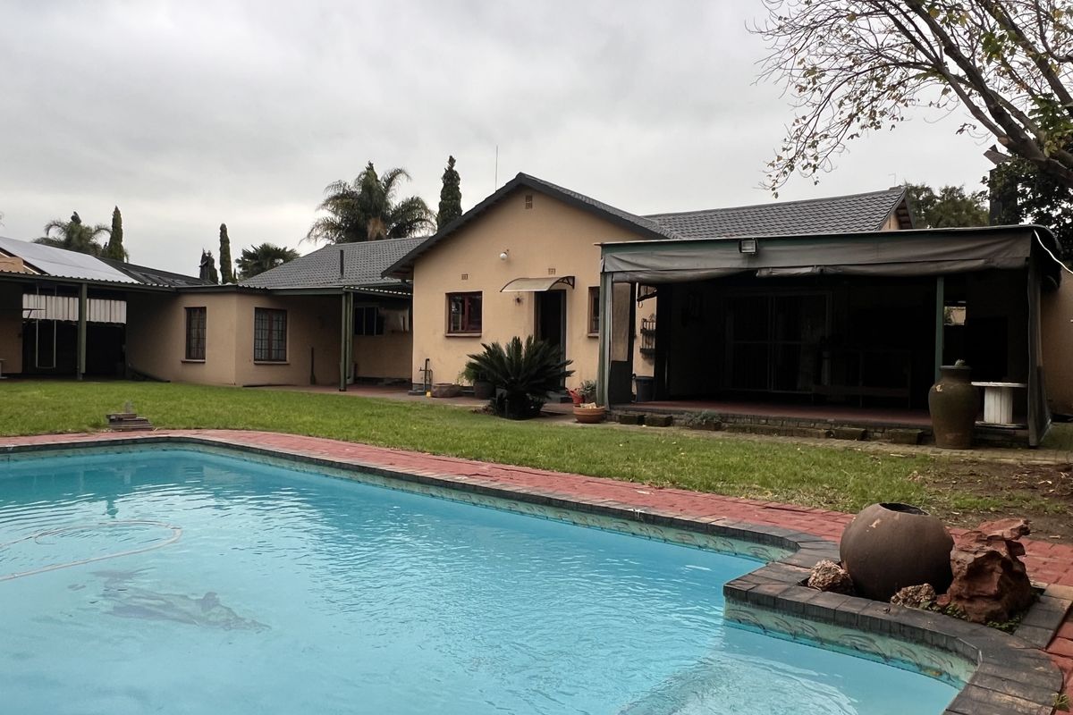Rear view of the property featuring a swimming pool, a covered patio area, and a spacious lawn.