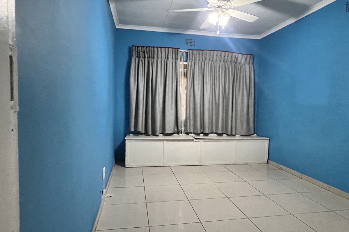 An empty bedroom featuring tiled flooring, a ceiling fan, and a built-in window seat with storage underneath.
