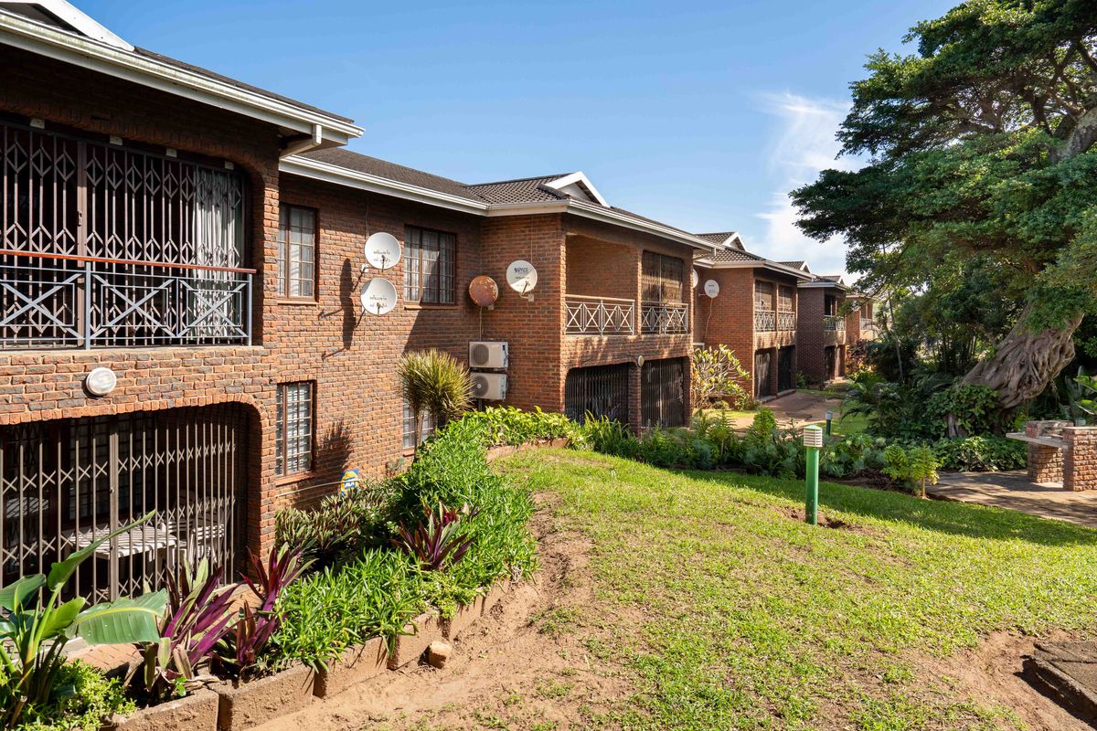 Rear view of a multi-story brick townhouse complex featuring private balconies, security gates, and established garden areas.