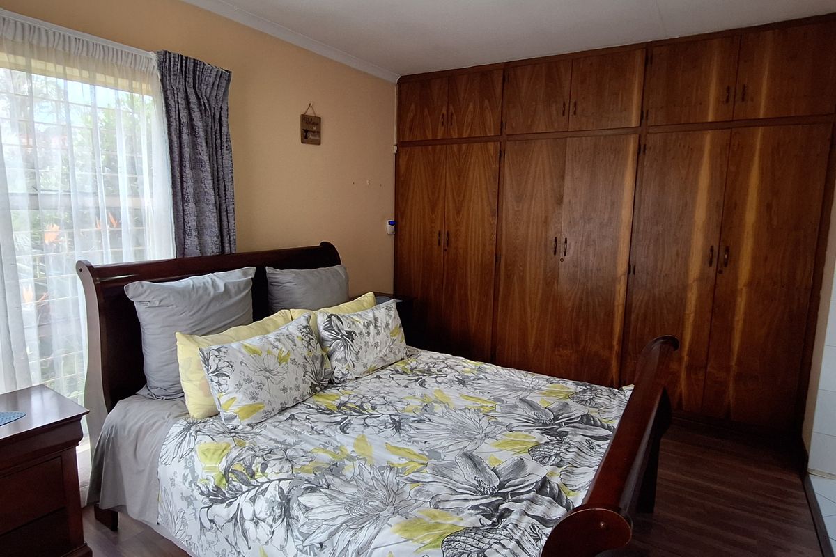 A bedroom featuring built-in wooden cupboards and laminate flooring, with a window providing natural light.