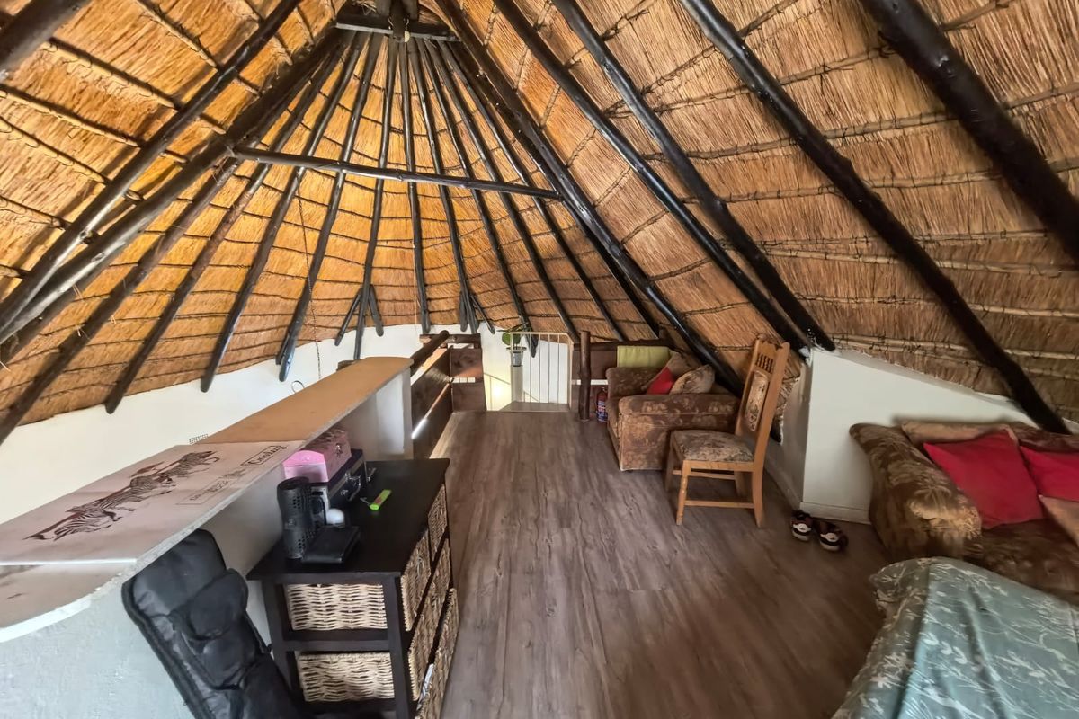 A loft-style bedroom featuring a high vaulted thatched roof with exposed timber rafters and laminate flooring, creating a rustic and cozy atmosphere.