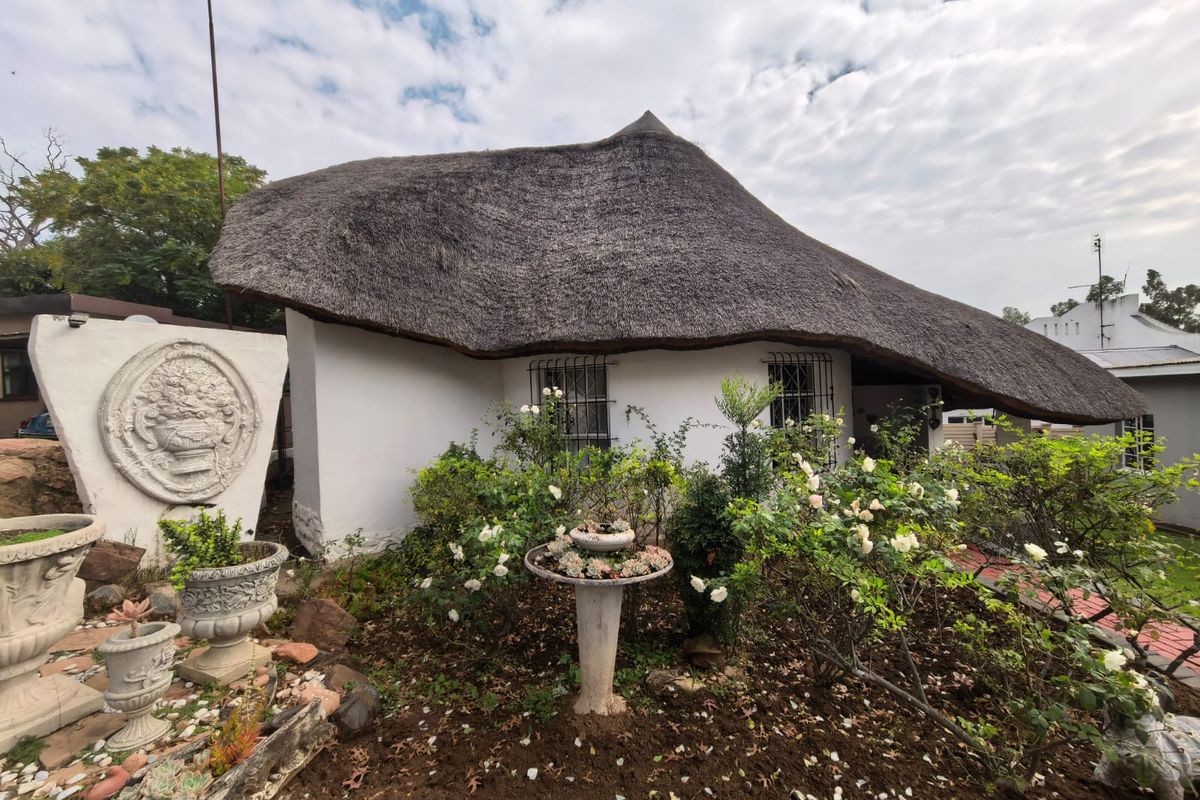 A charming townhouse exterior featuring a traditional thatched roof, white rendered walls, and established garden landscaping with decorative stone elements.
